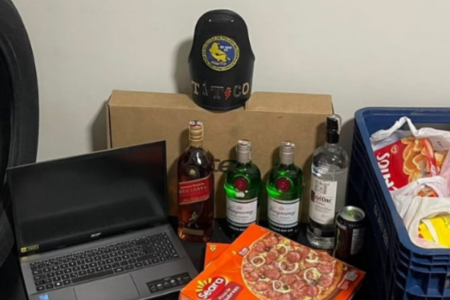 Imagem colorida mostra itens apreendidos na casa de um suspeito. Um notebook, uma garrafa de whisky, duas de gin e uma embalagem de pizza congelada estão entre os itens