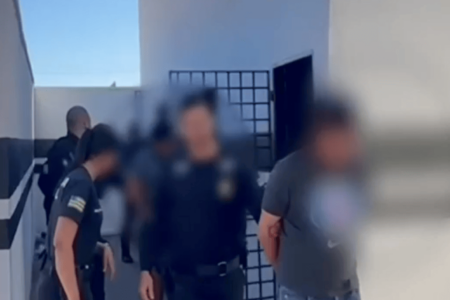 Imagem colorida mostra um agente da Polícia Civil levando um homem suspeito de crimes