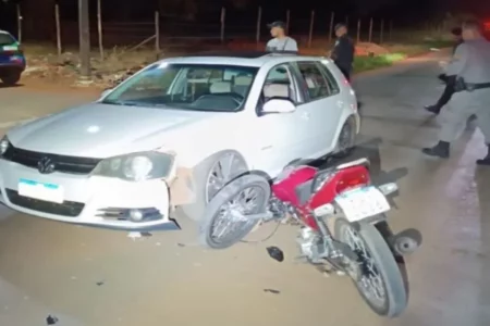 Imagem colorida mostra um carro branco e uma moto vermelha após uma colisão entre os dois