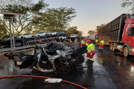 Imagem colorida mostra um carro totalmente destruído em uma rodovia após um acidente.