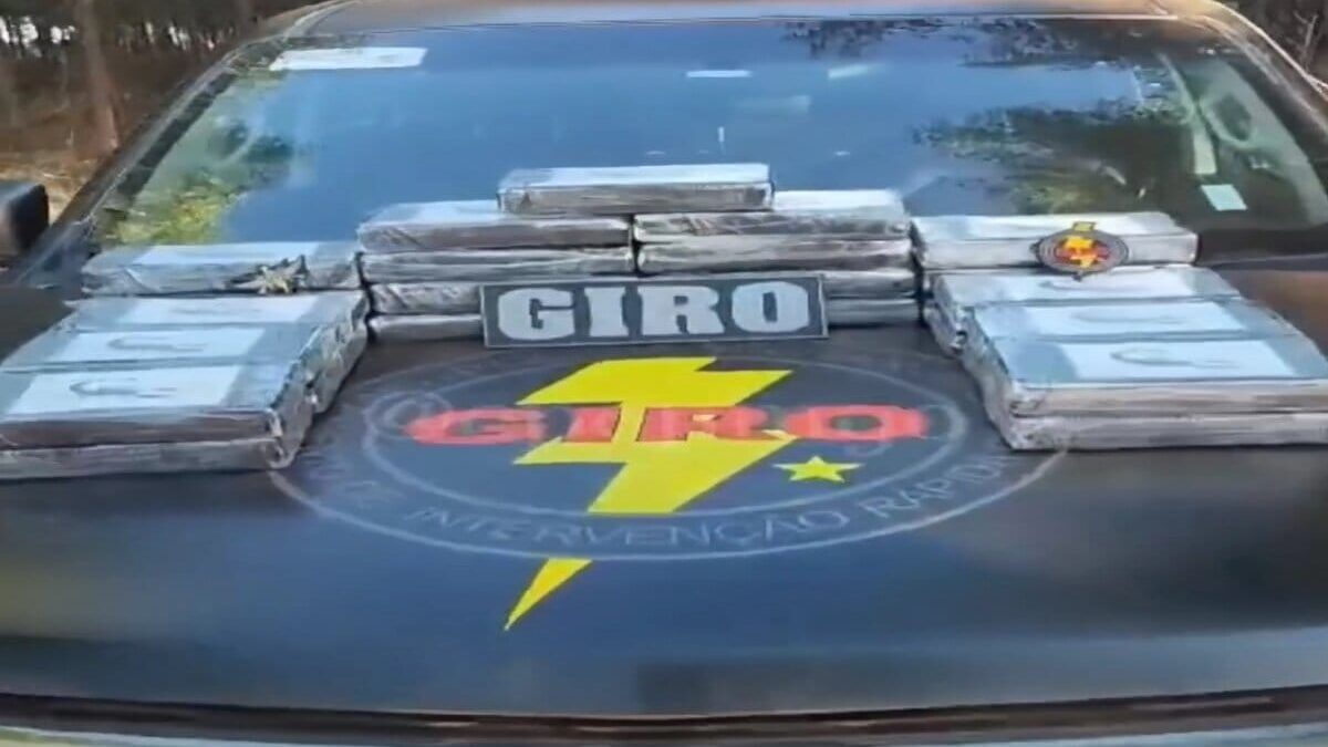 Imagem colorida mostra o capô de uma viatura da polícia com 27 pacotes de drogas em cima