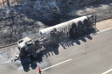 Imagem colorida mostra um caminhão tombado em uma rodovia após pegar fogo.