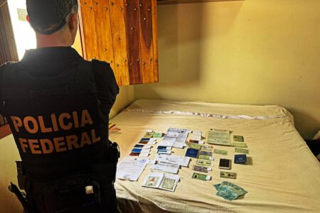 Imagem mostra um agente da policia de costas olhando para uma cama cheia de documentos