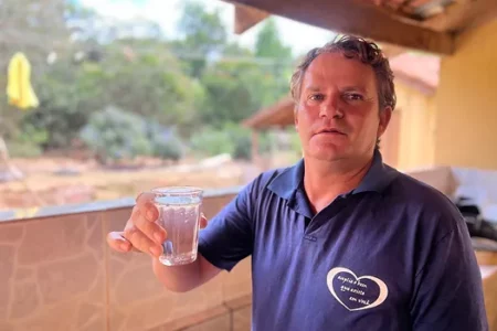 Imagem mostra um homem branco vestido em uma camisa azul e segurando copo com água