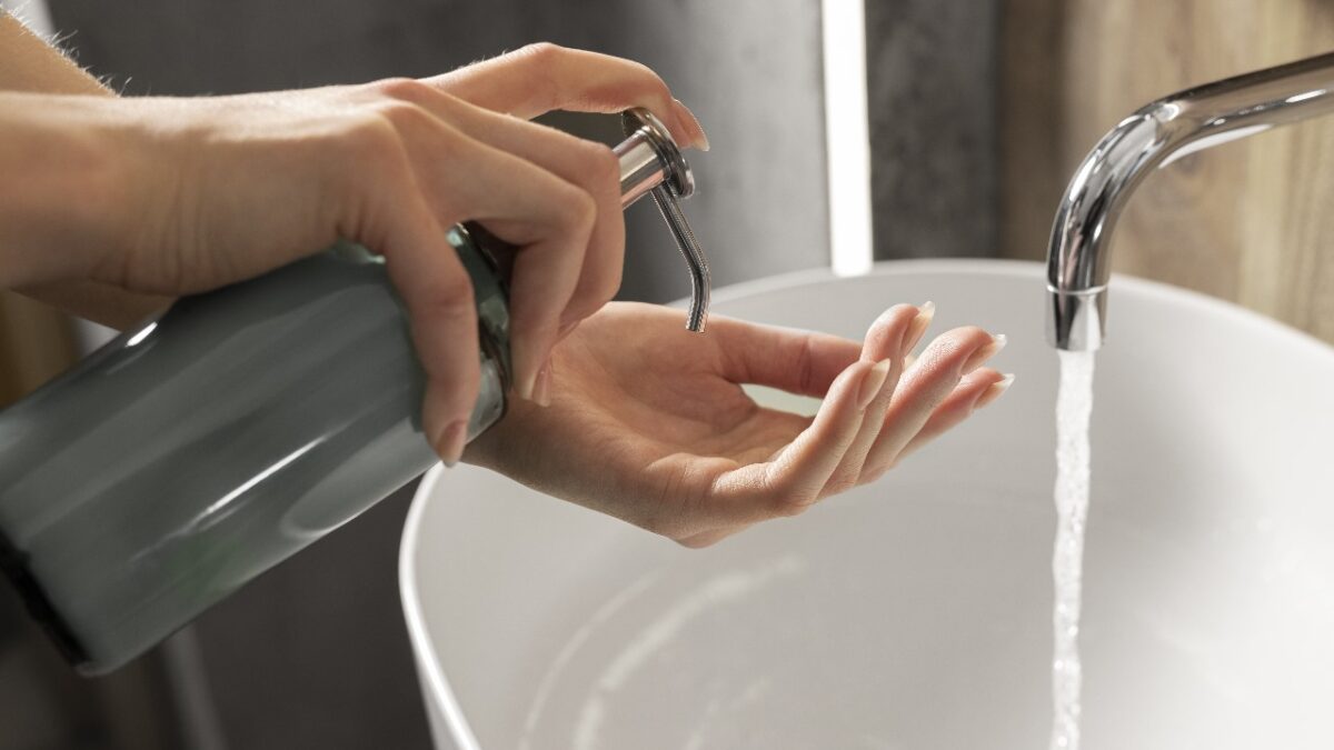 Imagem colorida mostra mãos de uma pessoa passando sabonete e uma torneira ligada.