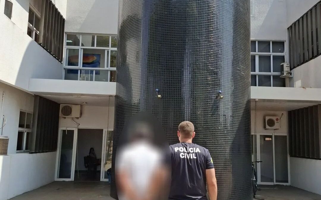 Imagem mostra a frente de uma delegacia e um agente da policia levando um homem preso