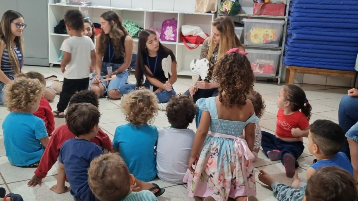 Imagem mostra uma sala de aula com professores e crianças