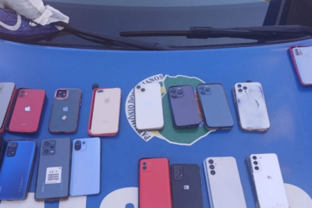 Imagem colorida mostra 17 celulares em cima do capô de uma viatura da Polícia Militar