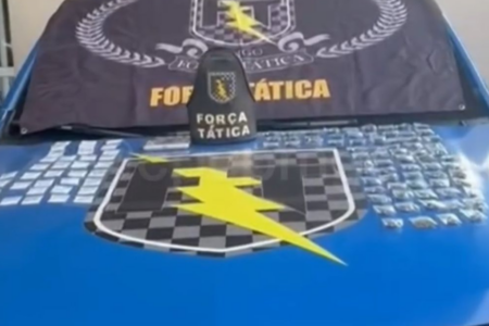 Imagem colorida mostra diversos pacotes de drogas em cima do capô de uma viatura da Polícia Militar.