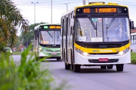 Imagem mostra dois ônibus do transporte coletivo passando um atrás do outro em uma rua