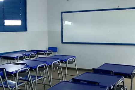 Imagem colorida mostra uma sala de aula com as mesas e cadeiras azuis e um quadro branco ao fundo.