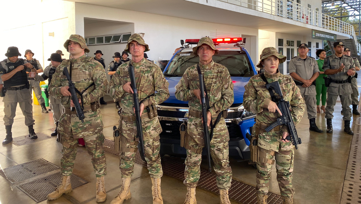 Imagem colorida mostra quatro policias do Batalhão Rural em frente a uma viatura da Polícia. Todos estão com armas nas mãos.