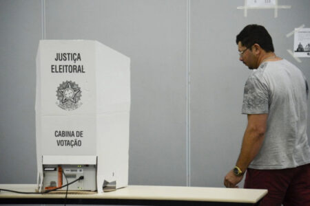 Imagem mostra um homem em pé, de lado, seguindo rumo à cabine de votação branca