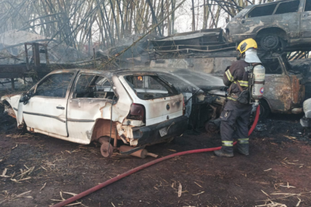 Imagem colorida mostra diversos carros queimados após um incêndio em um pátio.