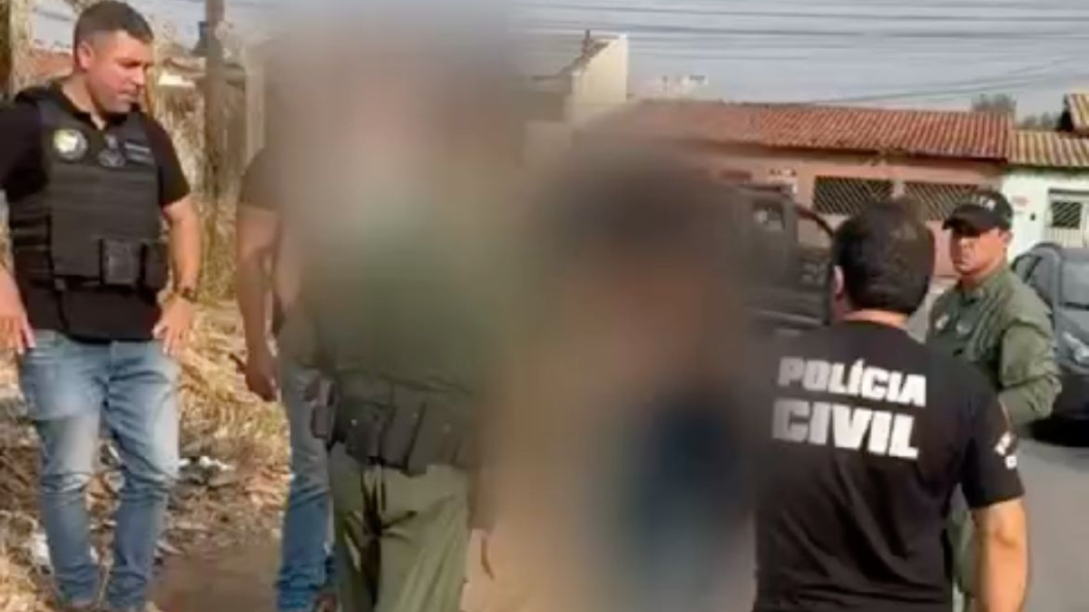 Imagem colorida e borrada mostra um homem sendo conduzido por dois policiais civis.