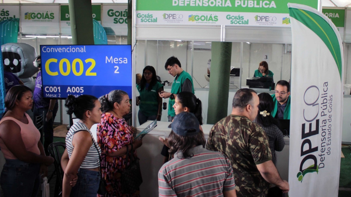 Imagem colorida mostra diversas pessoas em um stand da Defensoria Pública do estado de Goiás.