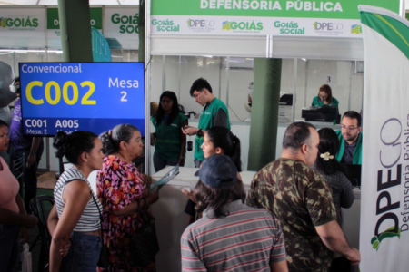 Imagem colorida mostra diversas pessoas em um stand da Defensoria Pública do estado de Goiás.