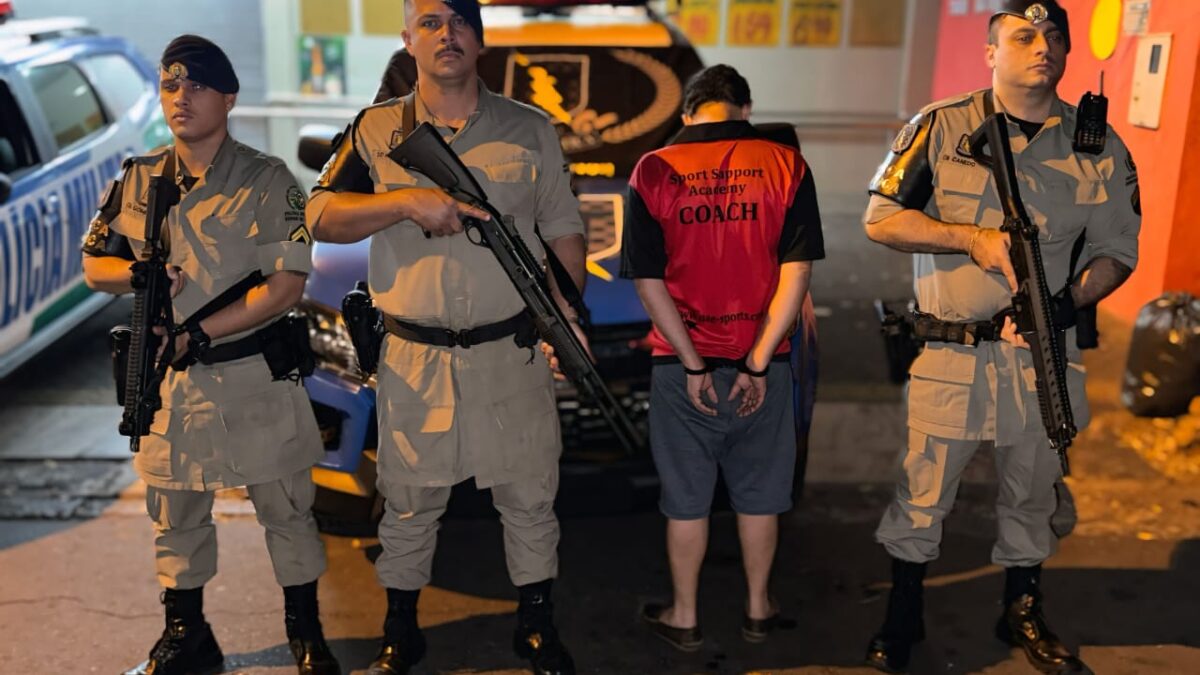 Imagem mostra um homem de costas ao lado de policiais armados