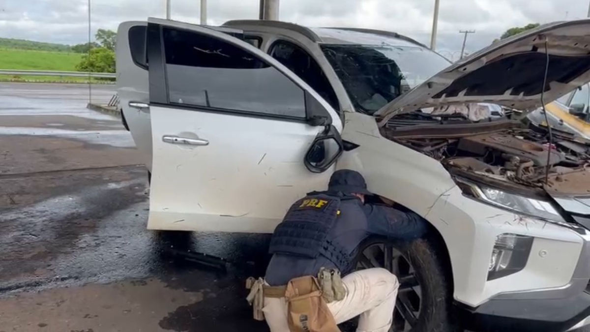 Imagem colorida mostra uma agente da Polícia Rodoviária Federal mexendo na roda de uma caminhonee.