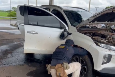 Imagem colorida mostra uma agente da Polícia Rodoviária Federal mexendo na roda de uma caminhonee.