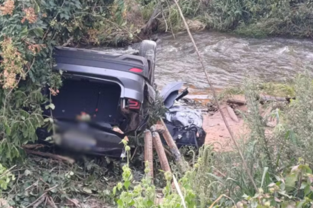 Imagem colorida mostra um carro cinza escuro de cabeça para baixo após um grave acidente.