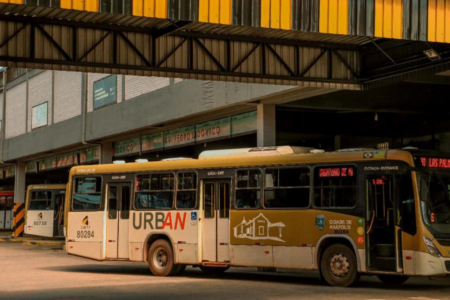 Imagem colorida mostra um ônibus do transporte coletivo parado em um terminal de ônibus.