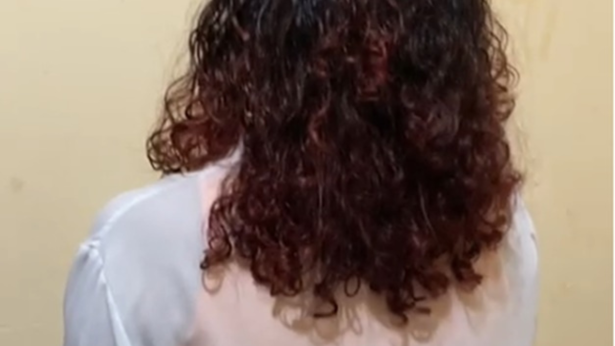 Imagem colorida mostra uma menina de costas. Na foto aparece só o cabelo dela, cacheado, e uma parte de sua camiseta branca.