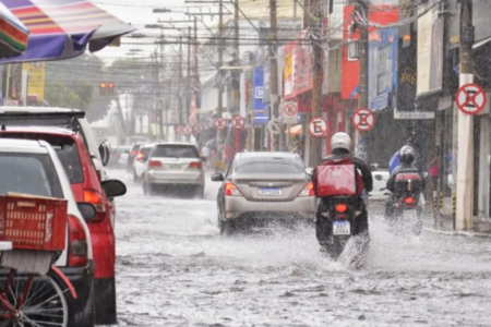 Imagem colorida mostra uma rua de Goiânia durante um dia de chuva com carros e motos passando.