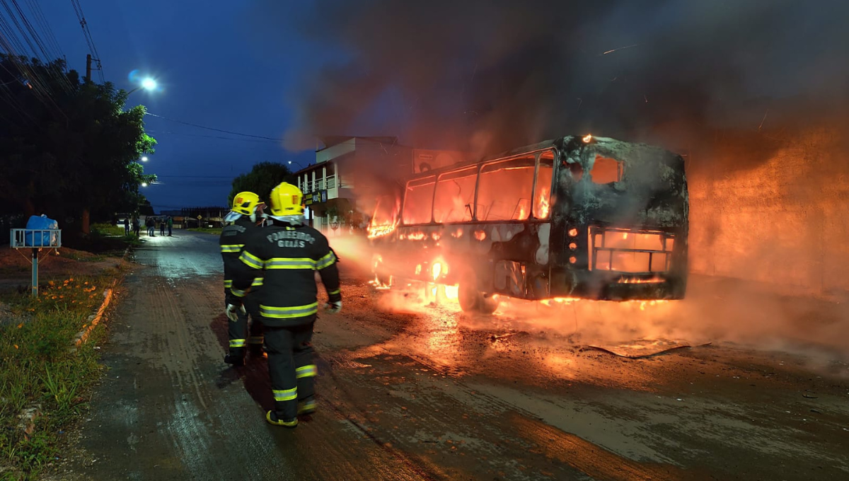 Imagem colorida mostra militares dos bombeiros combatendo um incêndio que atinge um micro-ônibus.