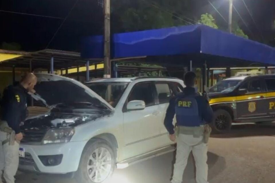 A imagem mosta dois policiais da PRF fazendo buscas em um veículo furtado
