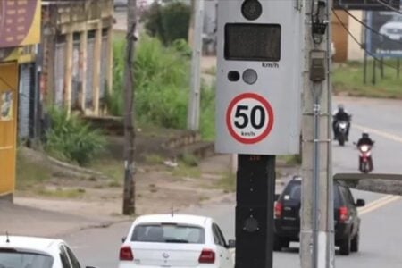 A imagem mostra o trânsito com vários carros descendo uma rua de Goiânia, com foto em um aparelho que fiscaliza a velocidade dos veículos