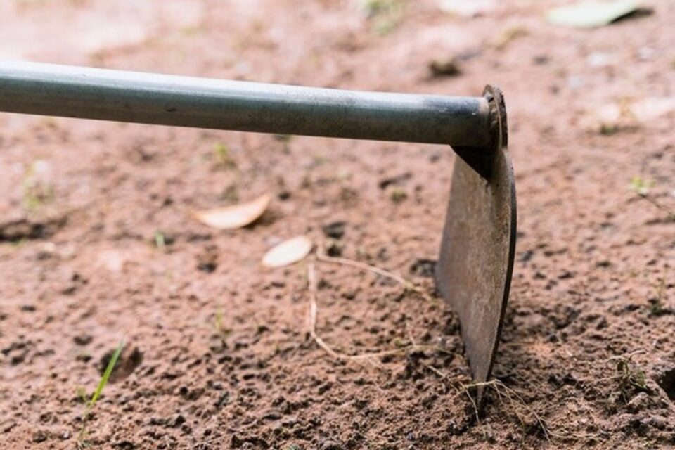A imagem mostra uma enxada batendo o solo de terra