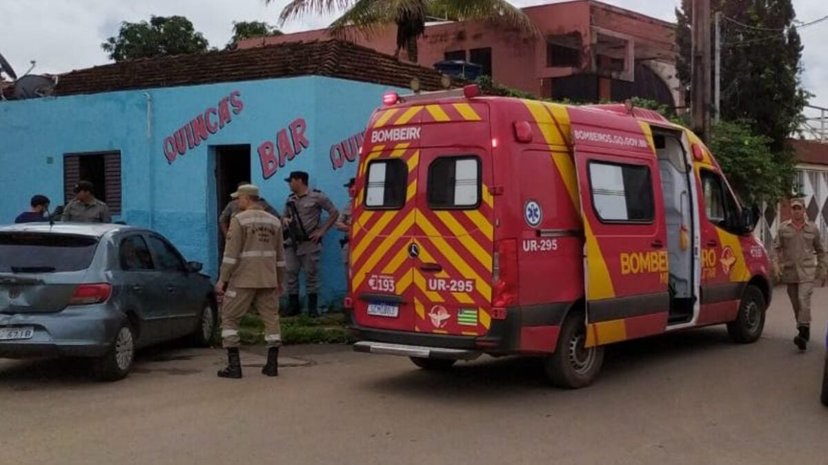 A imagem mostra uma ambulância do Corpo de Bombeiros estacionado ao lado de um bar, onde socorrem uma vítima de acidente