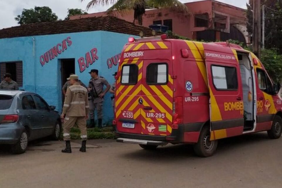 A imagem mostra uma ambulância do Corpo de Bombeiros estacionado ao lado de um bar, onde socorrem uma vítima de acidente