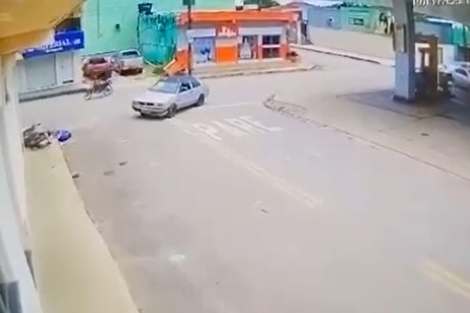 A imagem mostra um carro parado no meio da rua após o acidente e o casal de adolescentes que foram arremessados estão feridos sobre a calçada
