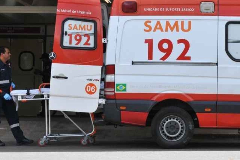 A imagem mostra uma unidade do Samu com um socorrista retirando uma maca do interior do veículo
