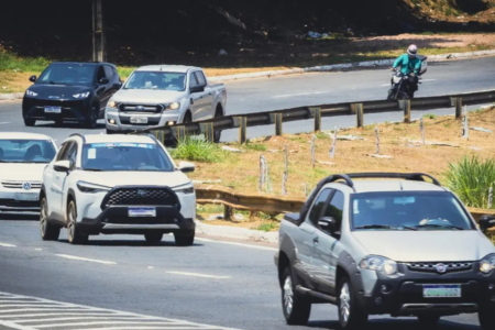 Imagem colorida mostra carros passando por uma rodovia.