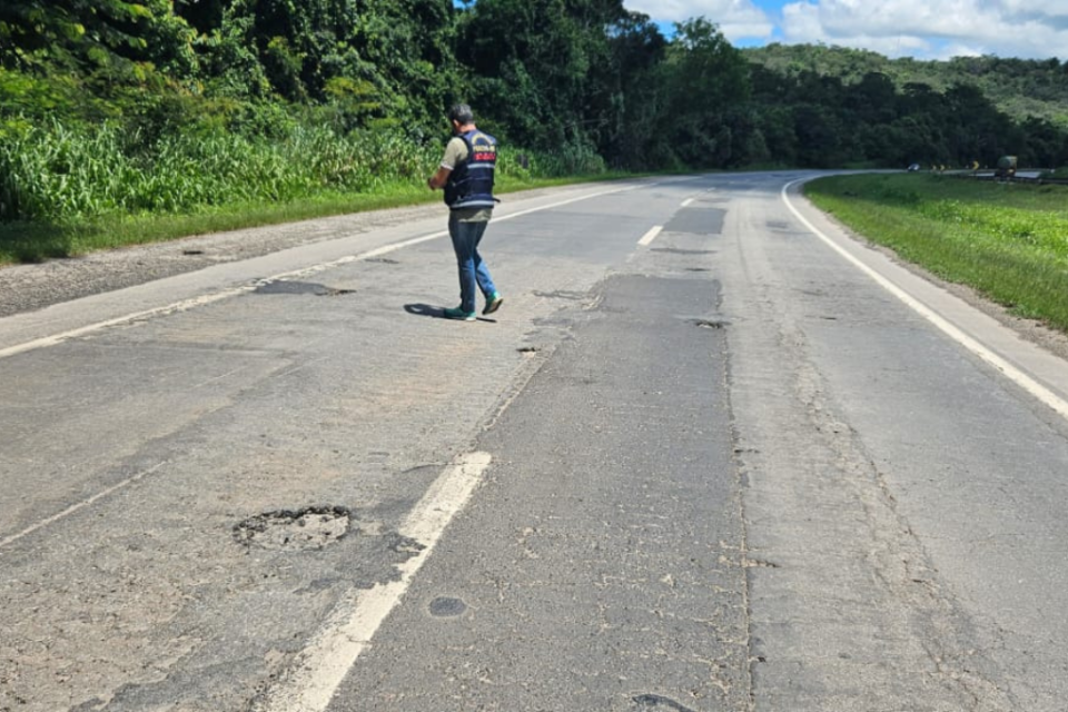 Imagem colorida mostra um trecho da BR-153 com buracos e um fiscal do Procon Goiás.