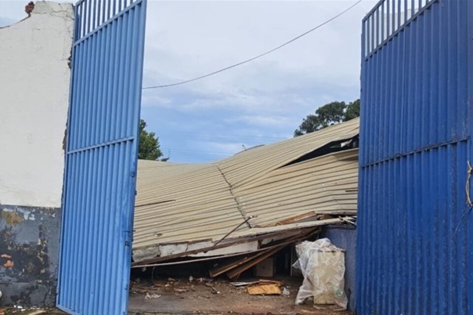A imagem mostra um portal de cor azul aberto e no interior do imóvel um telhado de zinco que desabou durante temporal