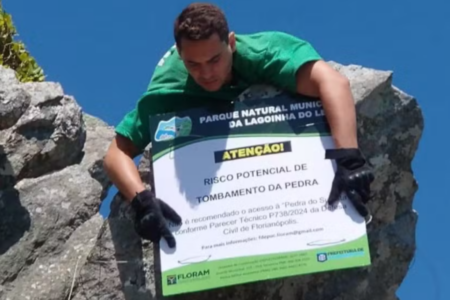 Um homem colocando a placa que limita o acesso ao ponto turístico