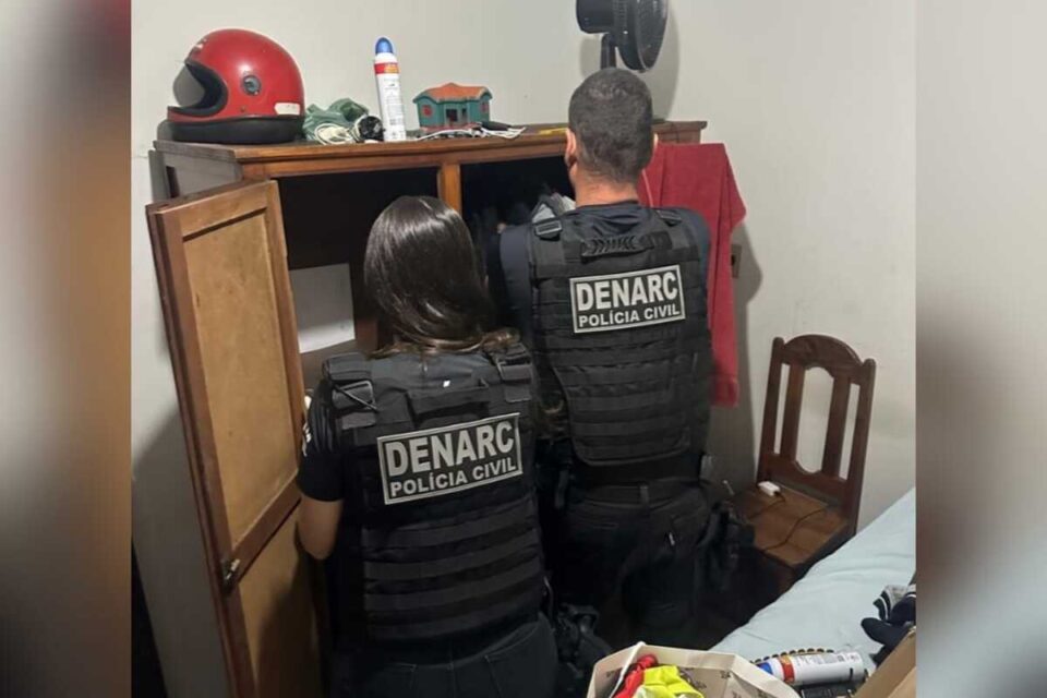 A imagem mostra dois agentes da Polícia Civil fazendo buscas em um armário de madeira em uma das residências da operação