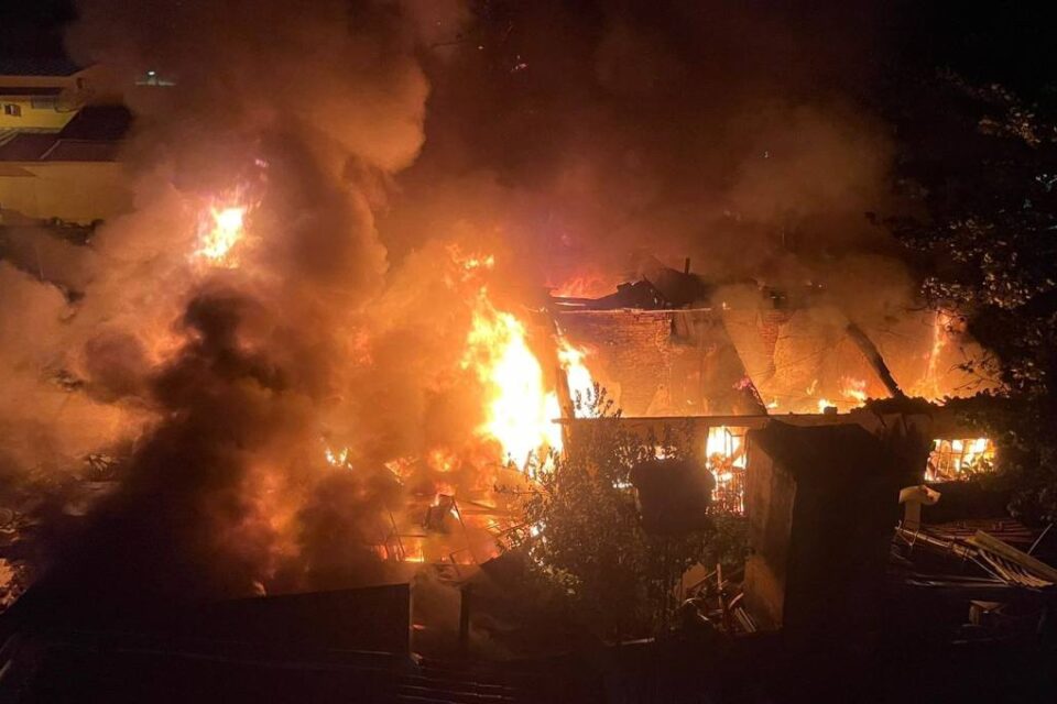 Imagem colorida do alto mostra uma casa pegando fogo e completamente destruída.