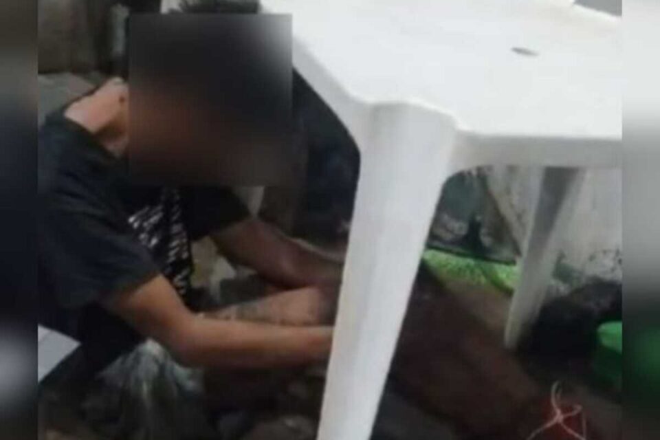 A imagem mostra um jovem suspeito de furto amarrado ao lado de uma mesa de plástico aguardando a chegada da polícia