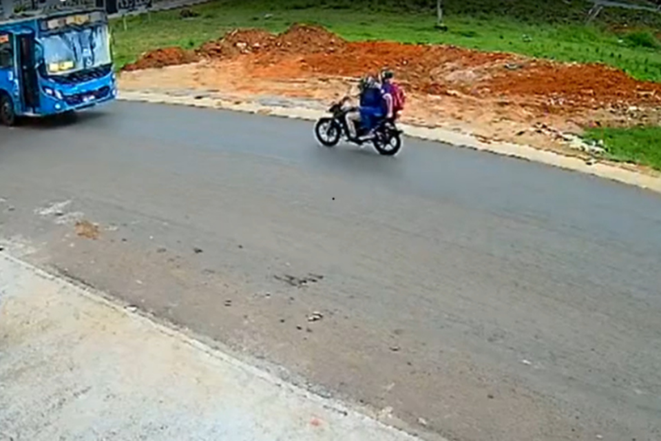 Imagem colorida mostra uma moto e um ônbus em uma rodovia em sentidos opostos antes de um acidente.