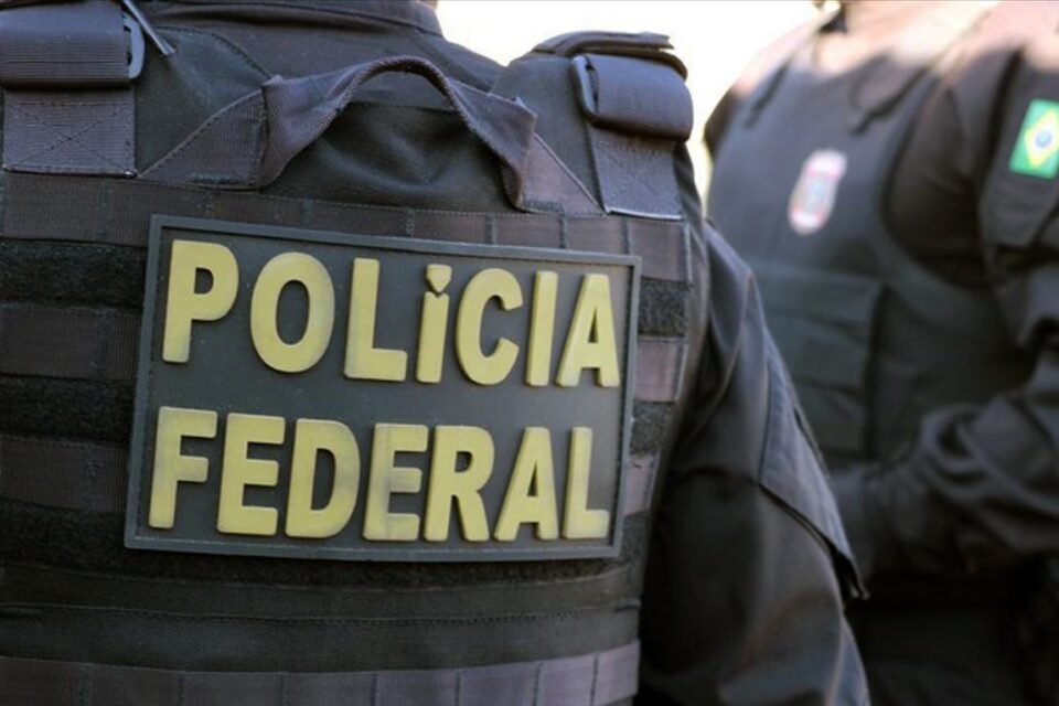 A imagem mosta o uniforme de um policial federal de costas