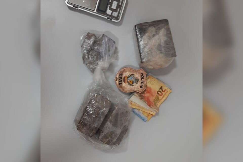 A imagem mostra apreensão realizada pela polícia, nos quais sobre uma mesa estão drogas, balança e dinheiro