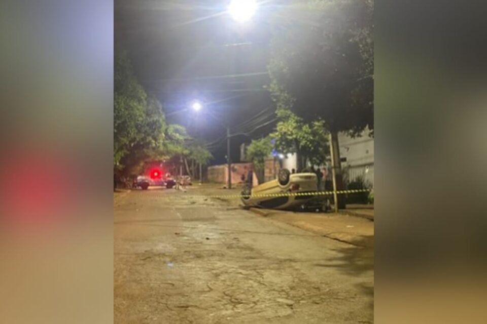A imagem mostra o carro capotado sobre a motocicleta em cima de uma calçada