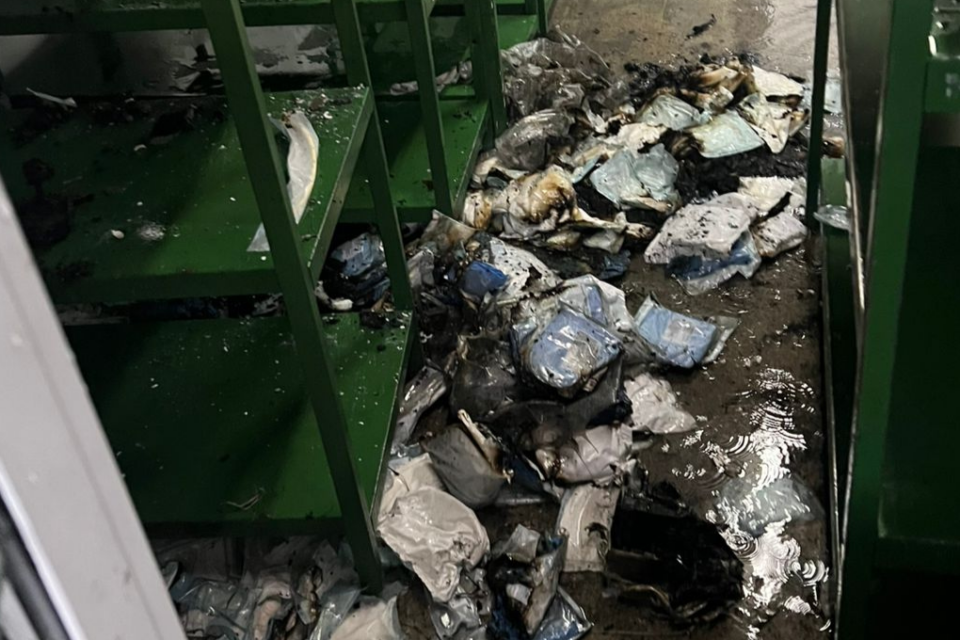 Imagem colorida mostra uma sala destruida após um incêndio com prateleiras verdes e muito material no chão.