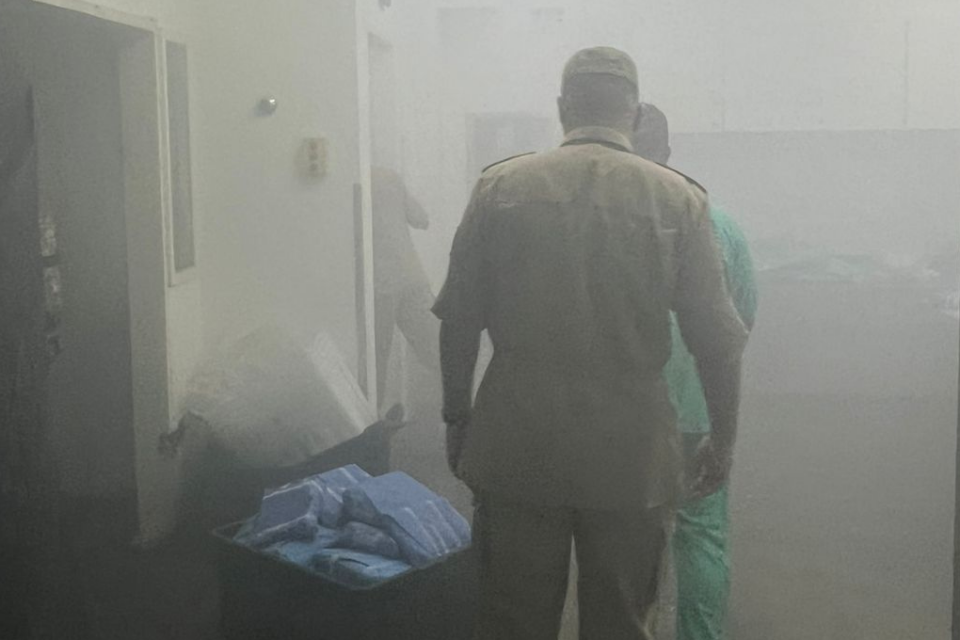 Imagem colorida mostra um bombeiro militar de costas em meio fumaça após um incêndio