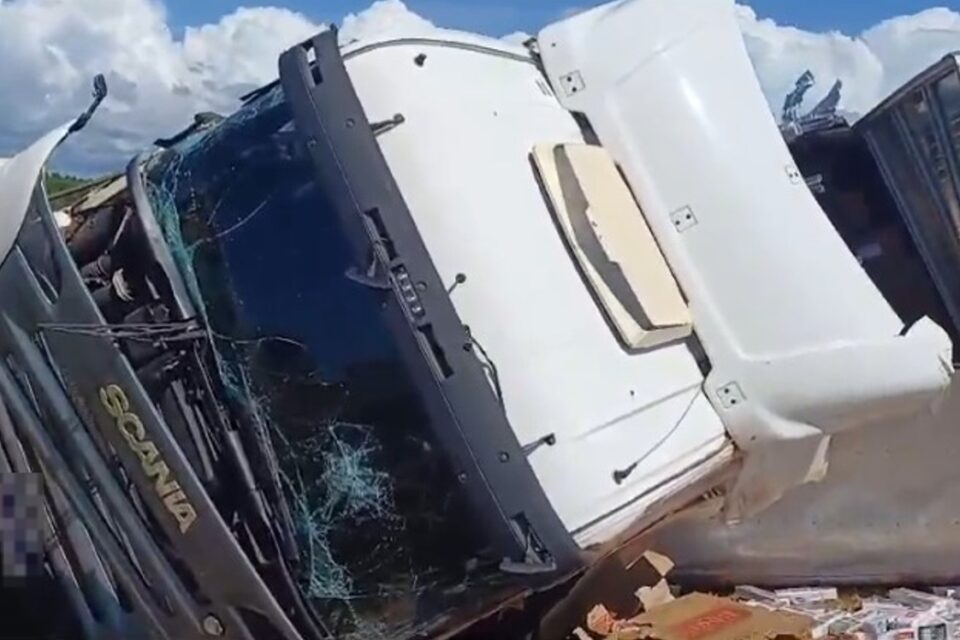 A imagem mostra um caminhão tombado, com a frente destruída após o acidente
